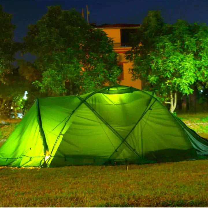 Green camping tent illuminated at night in a grassy area with trees.