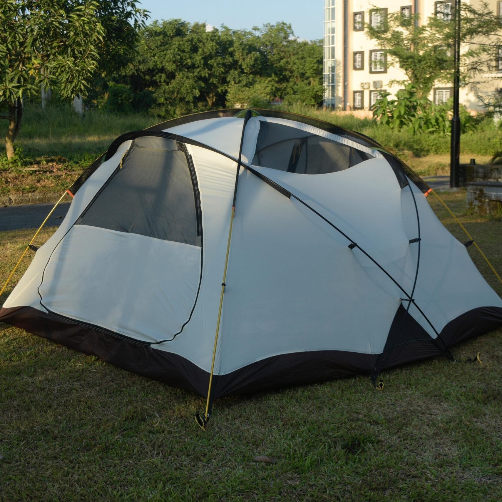 White camping tent with black accents on grass near a building